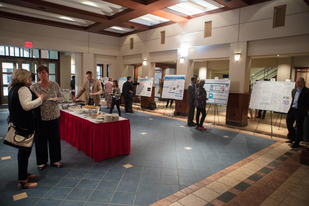The Graduate Showcase, including many posters, a buffet table, and people moving around the room